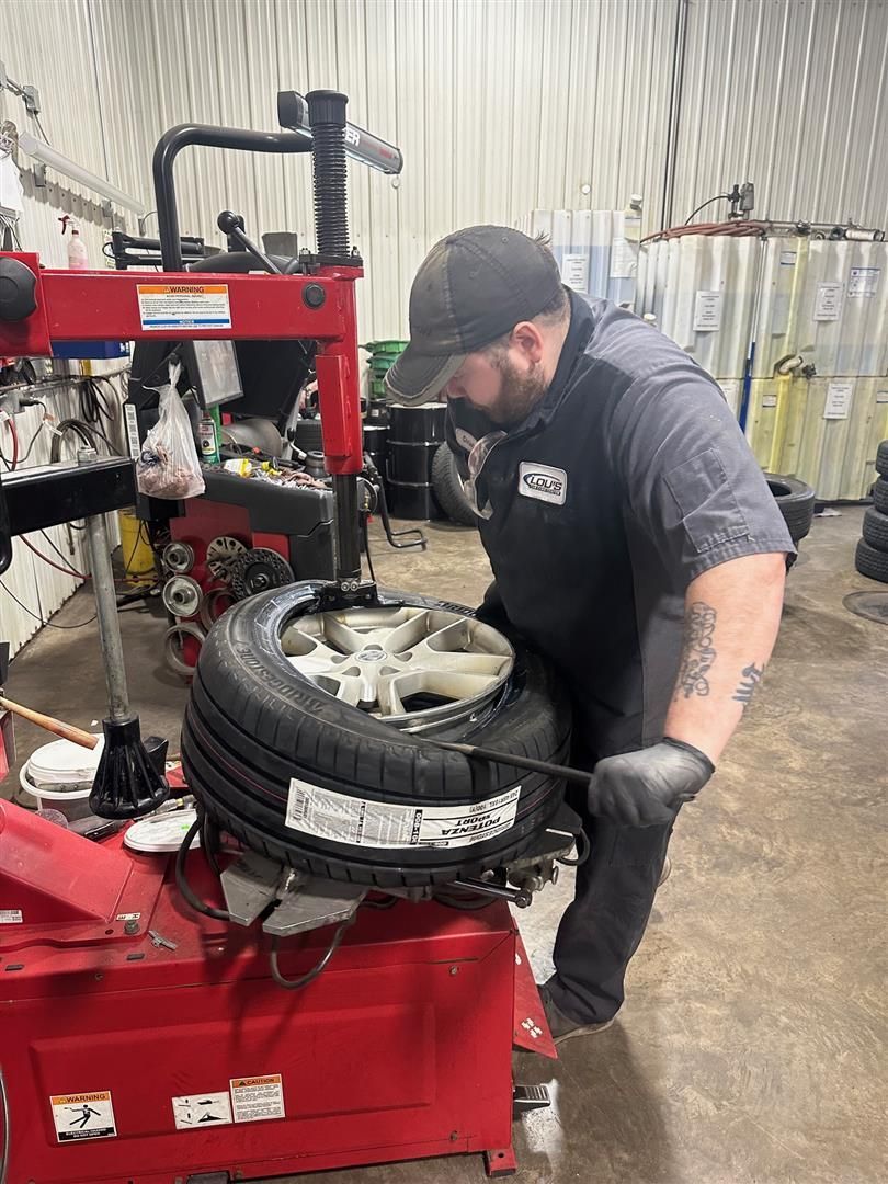 A man is changing a tire on a machine in a garage. | Lou's Car Care Center, Inc.