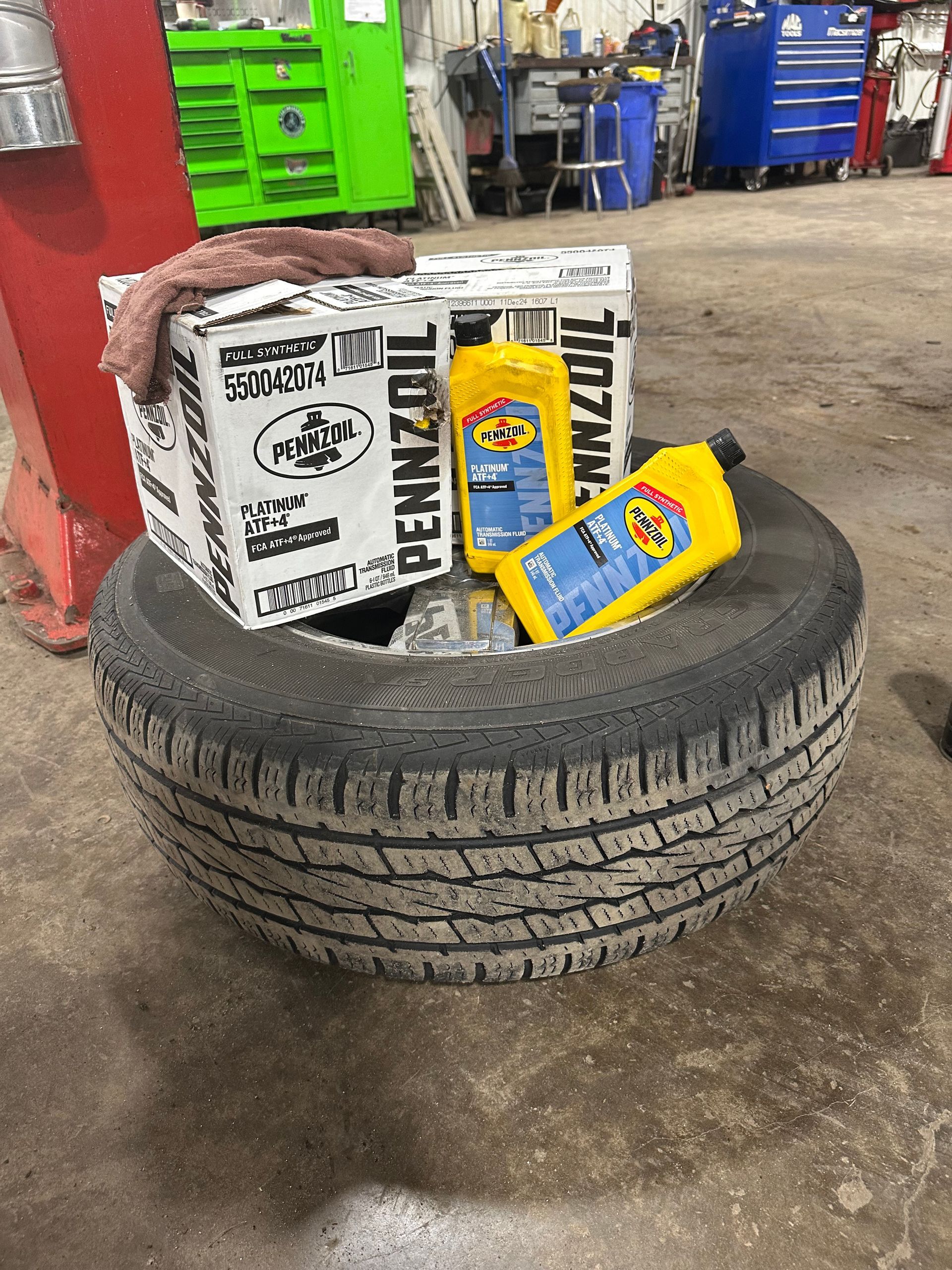 Pennzoil motor oil bottles and box on top of a vehicle tire in shop.