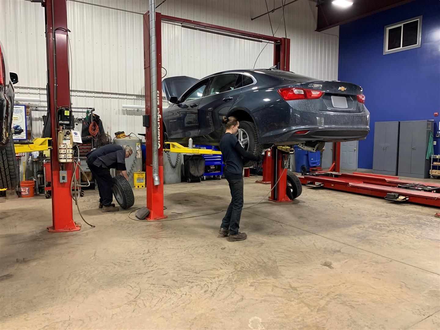 A man is working on a car on a lift in a garage. | Lou's Car Care Center Inc.