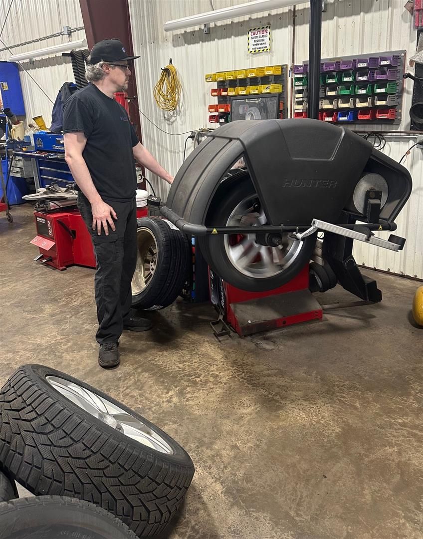 A man is standing next to a tire balancing machine in a garage. | Lou's Car Care Center, Inc.