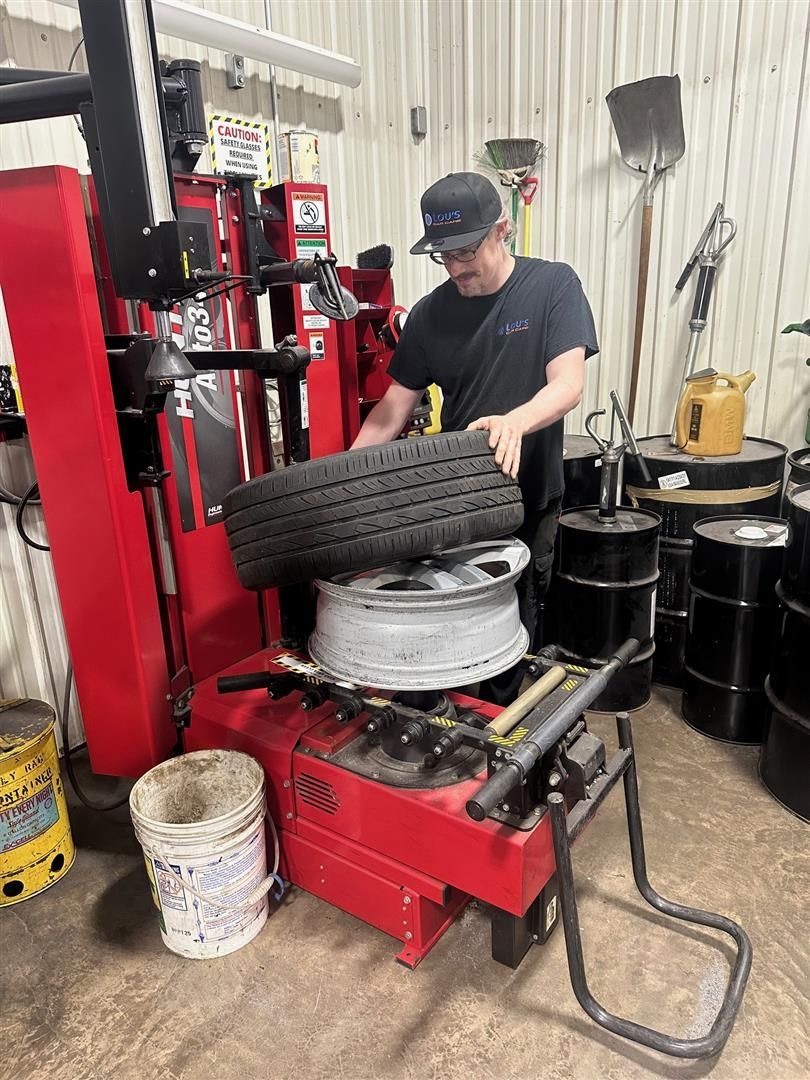 A man is changing a tire on a machine in a garage. | Lou's Car Care Center, Inc.