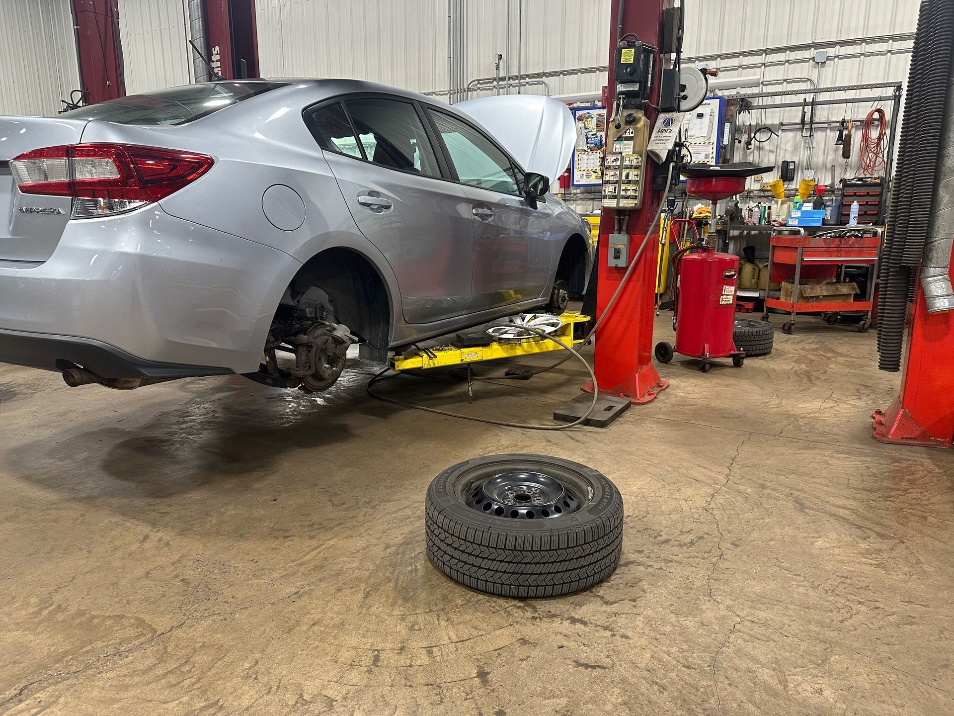 A car is sitting on a lift in a garage next to a tire. | Lou's Car Care Center, Inc.