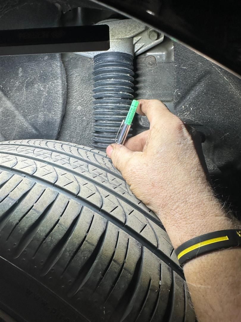 A person is holding a green marker over a tire. | Lou's Car Care Center, Inc.