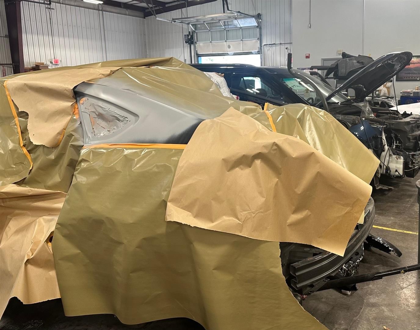 A car is covered in plastic wrap in a garage. | Lou's Car Care Center, Inc.
