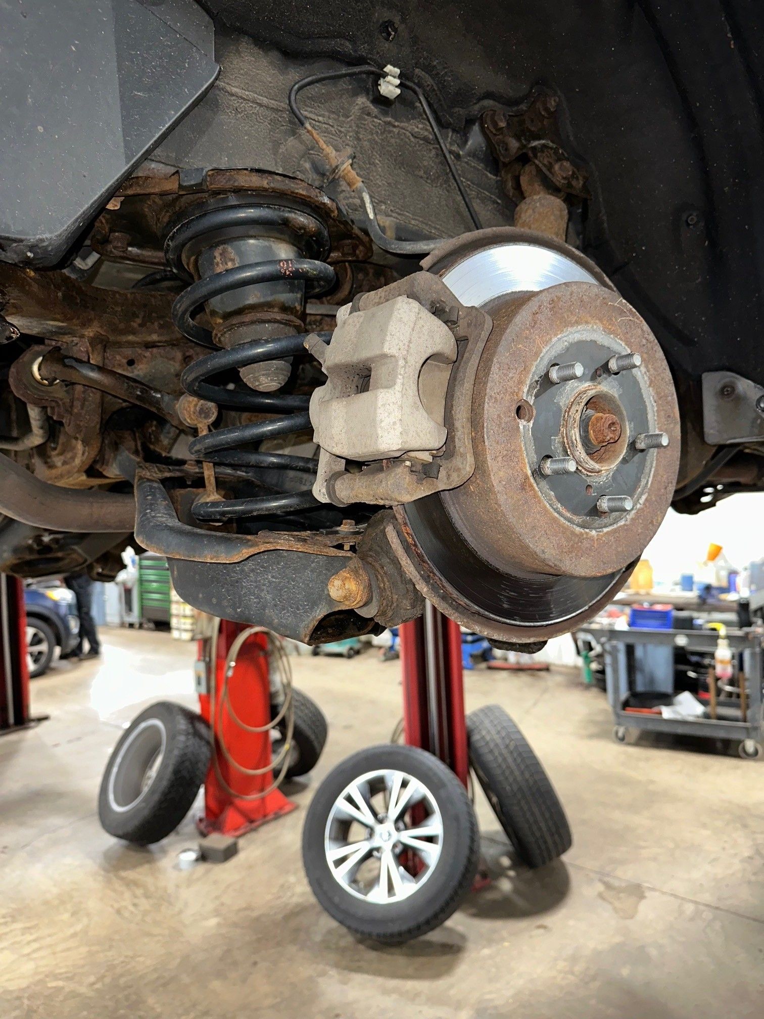 A black coils spring and brakes on a vehicle in the shop. Vehicle tires are laying against red vehicle lifts in the background. | Lou's Car Care Center, Inc.