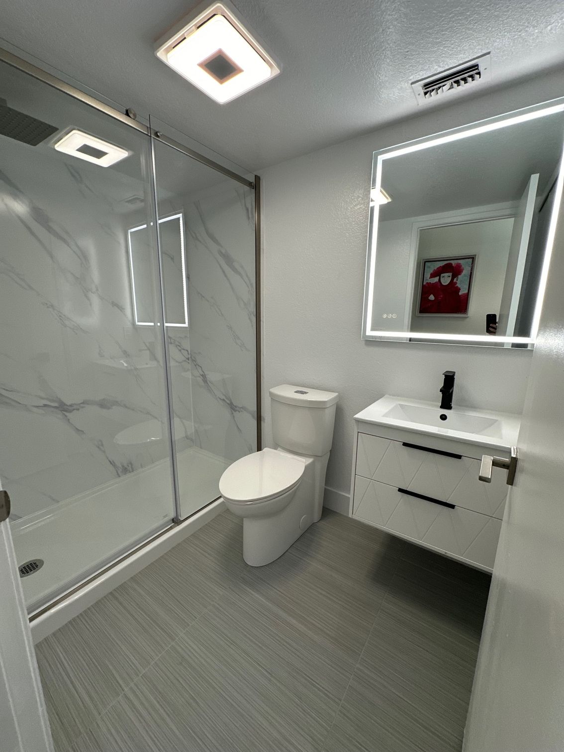 Modern bathroom with glass shower, floating vanity, and gray floor tiles.