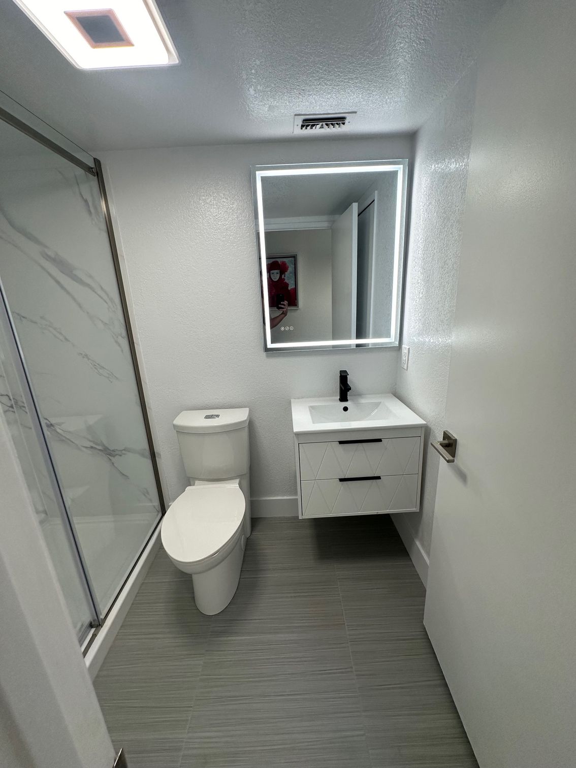 Small modern bathroom with a toilet, floating vanity, lit mirror, and marble shower.