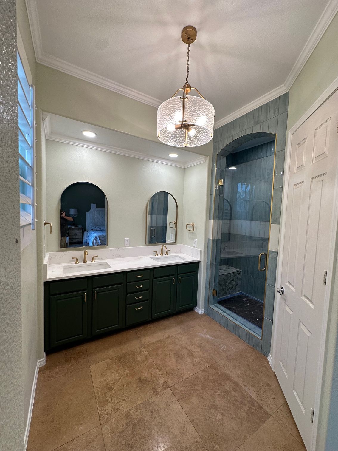 Bathroom with green vanity, gold accents, glass shower, and patterned floor.