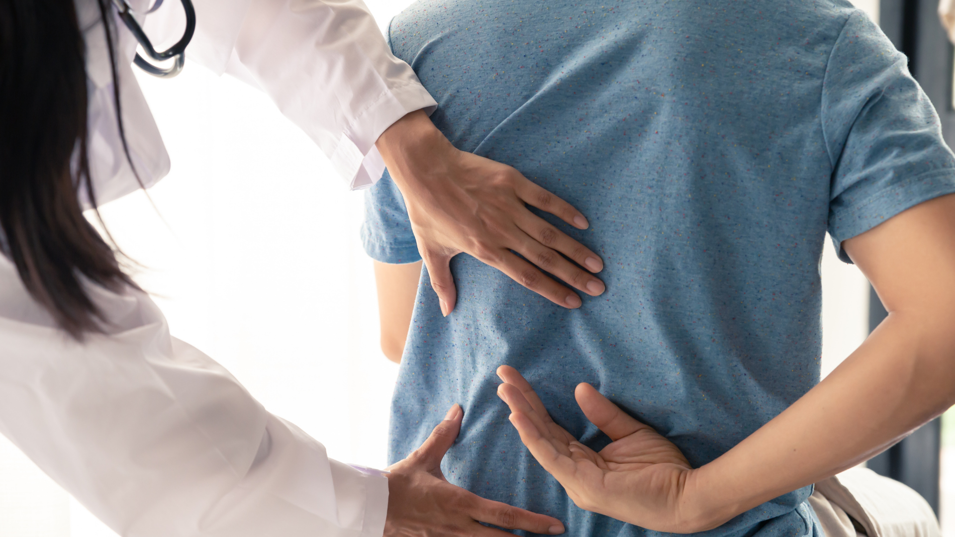 Healthcare worker examining a seated patient's lower back with both hands