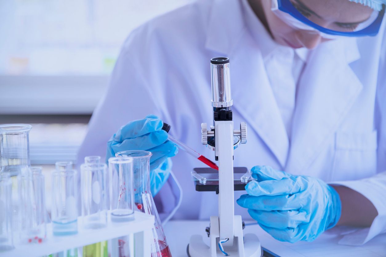 Lab worker in a white coat and blue gloves using a pipette with a microscope.