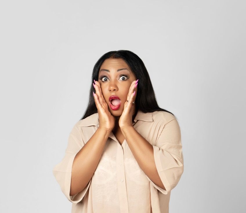 Woman with long black hair, surprised expression, hands on cheeks, mouth open.
