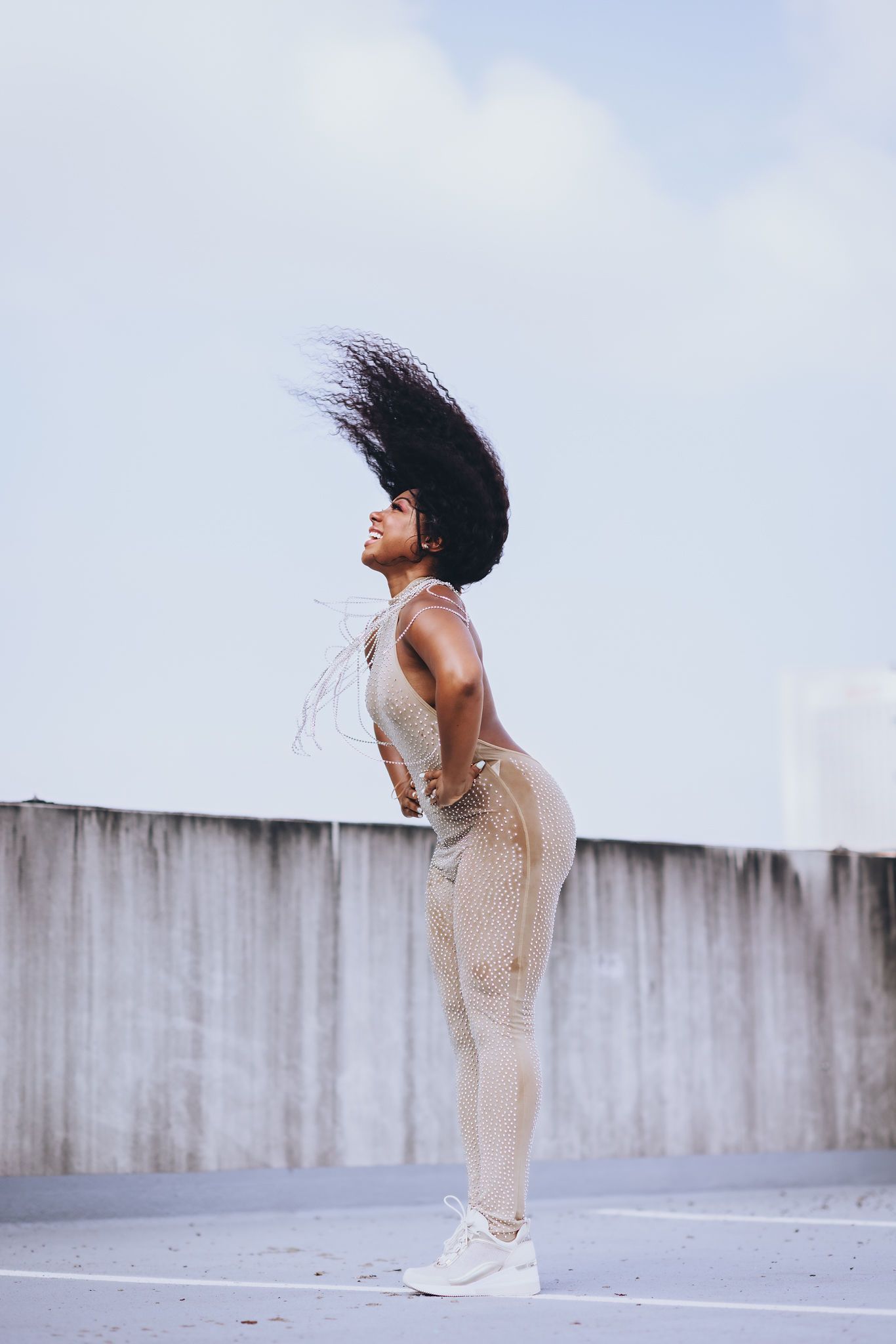 Woman with dark hair, back arched, in sparkly jumpsuit, on a rooftop; hair is in motion.