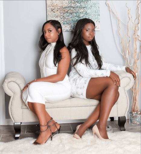 Two women in white dresses sitting back to back on a decorative bench.