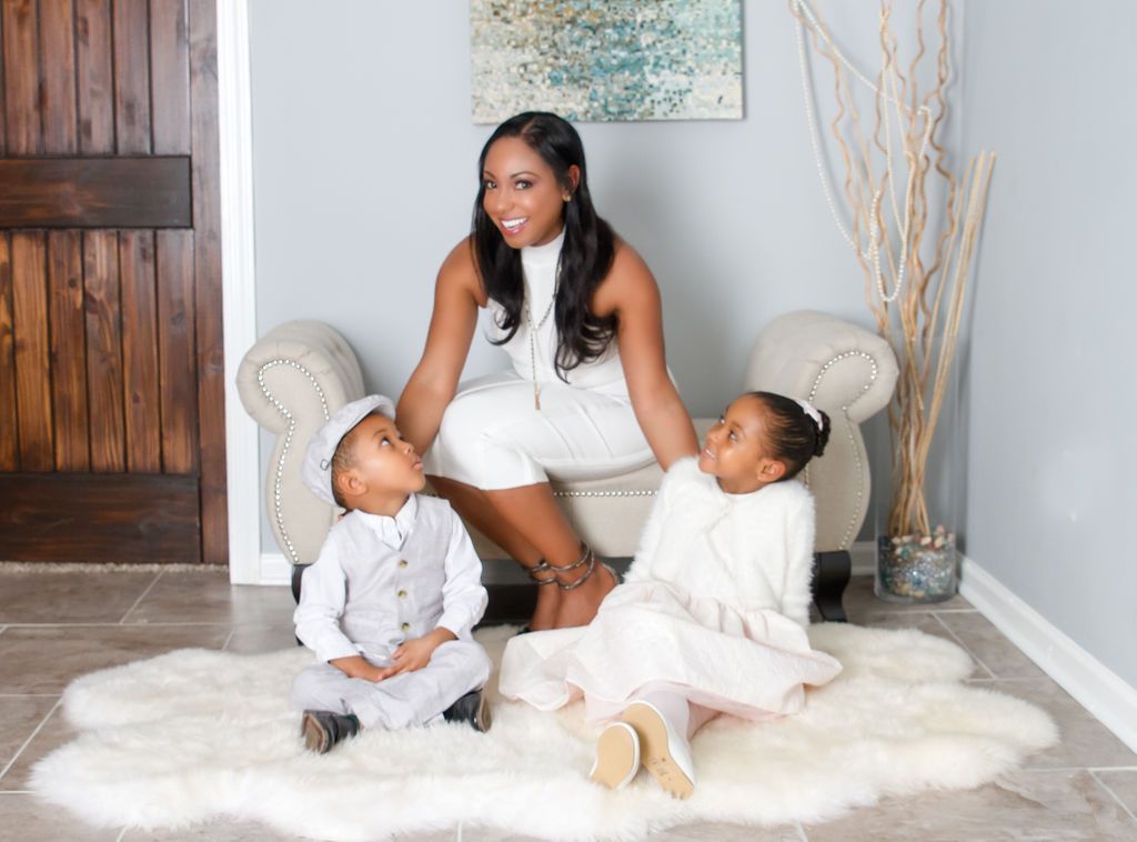 Woman and two children on rug, seated near wall. Woman smiles.