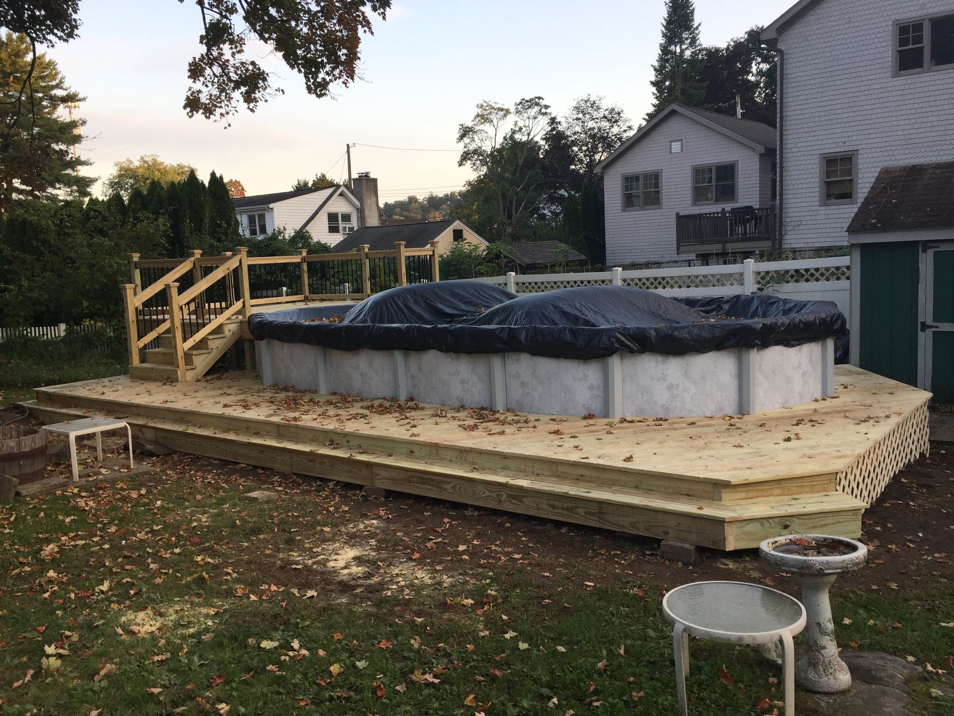 A partially built wooden deck surrounds an above-ground pool covered with a tarp. A set of wooden stairs is present.