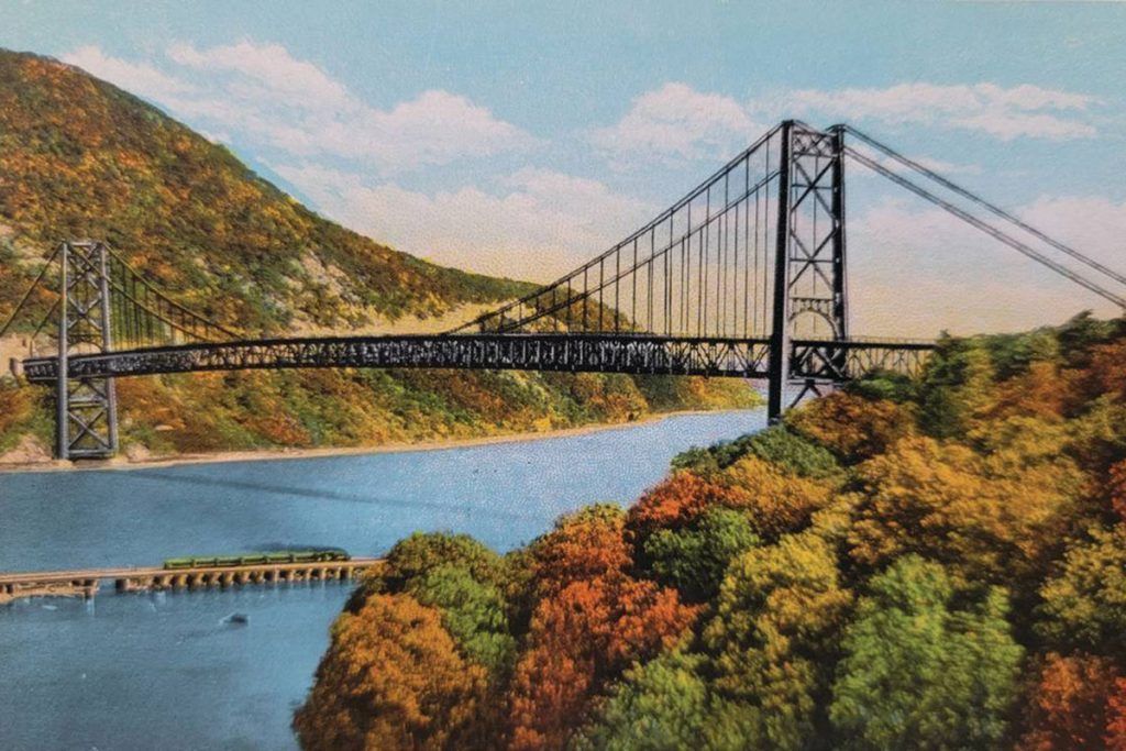 Suspension bridge over a river, with forested hills and autumn foliage.