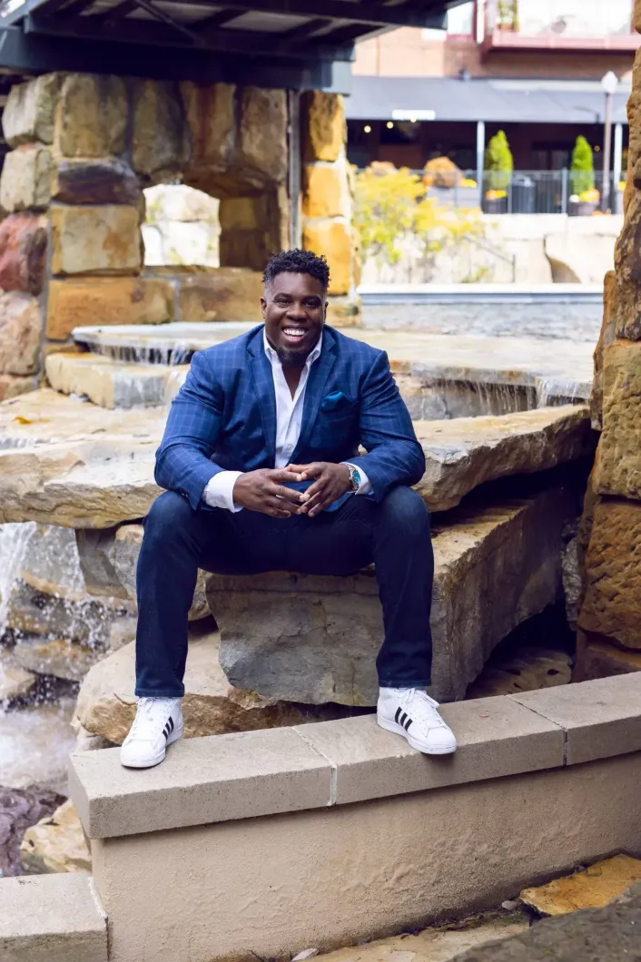 A man in a suit is sitting on a rock in front of a waterfall.