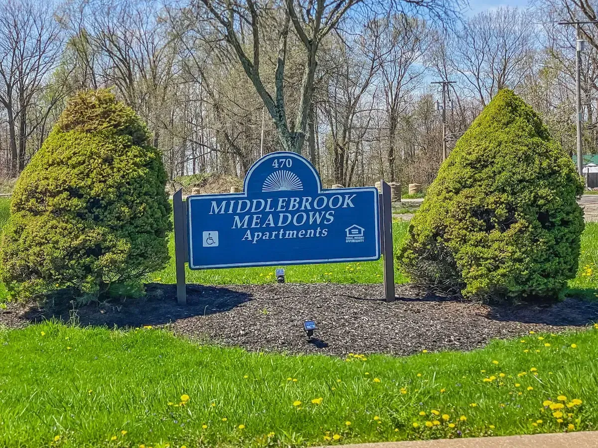 A sign for middlebrook meadows apartments is in the middle of a lush green field.
