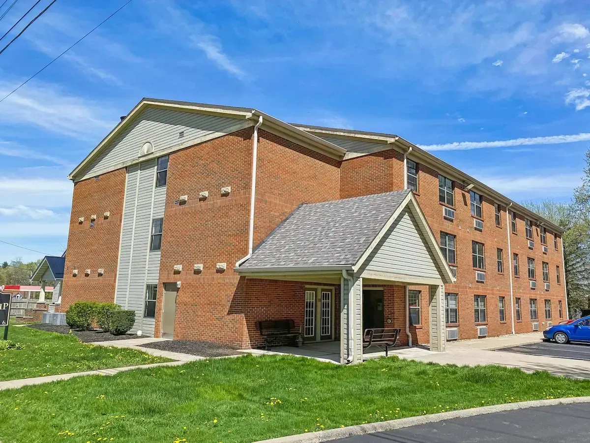 A large brick apartment building with a porch and a blue car parked in front of it.