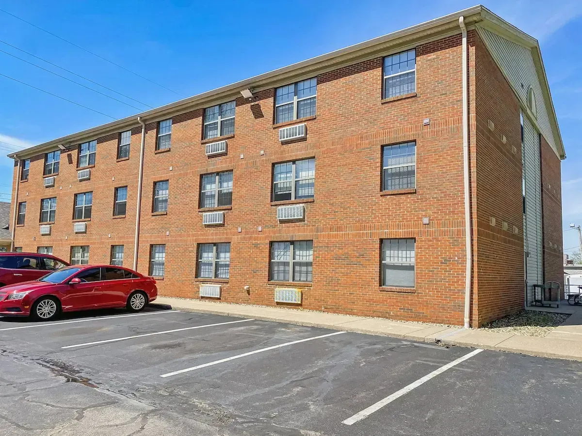 A red car is parked in front of a large brick apartment building.