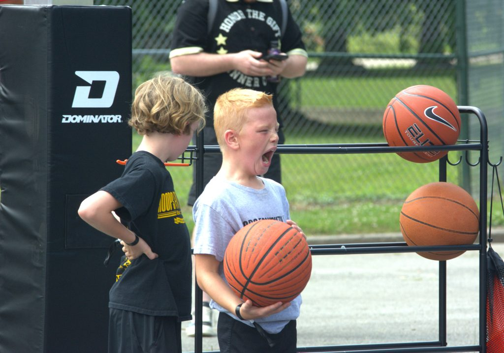 Two young boys are holding basketballs in front of a basketball rack.