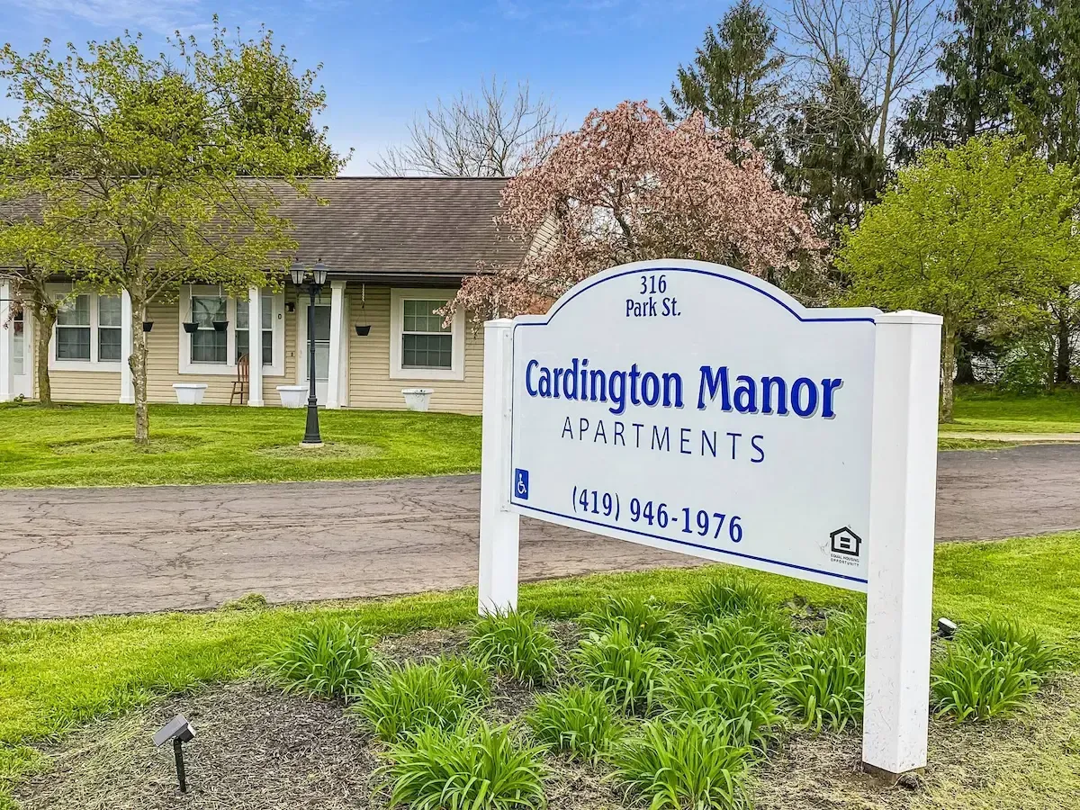 A sign for cardington manor apartments is in front of a house