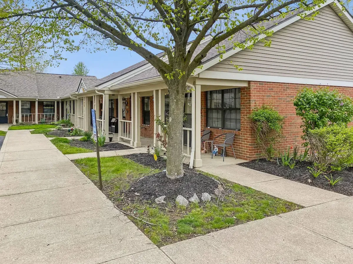 A brick house with a porch and a tree in front of it.