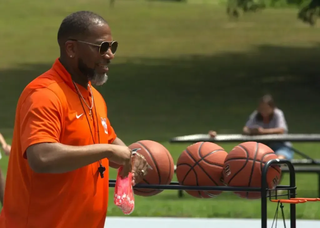 A man in an orange shirt is putting basketballs on a rack.