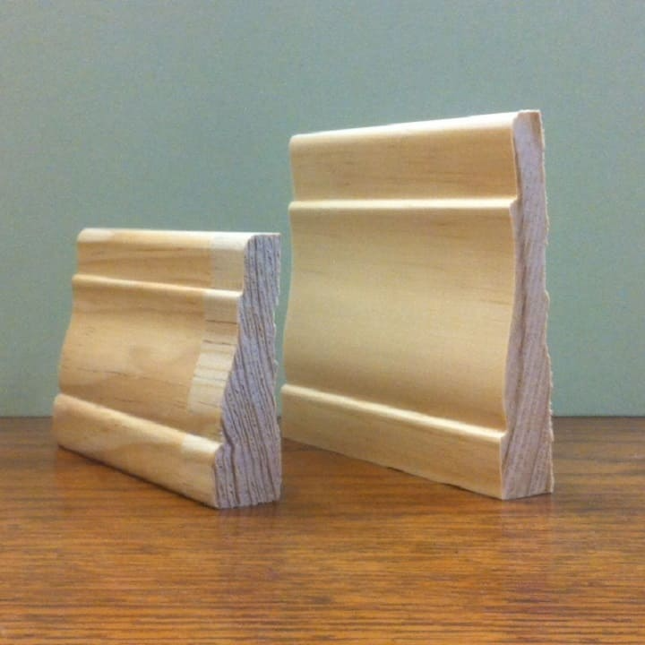 Two wooden baseboard samples, light-colored and decorative, on a wooden surface.