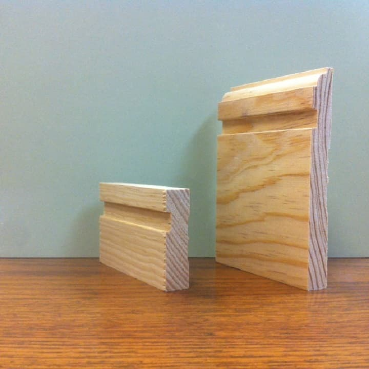 Two wooden molding samples on a wooden table. One is a small, the other is larger with a decorative top.