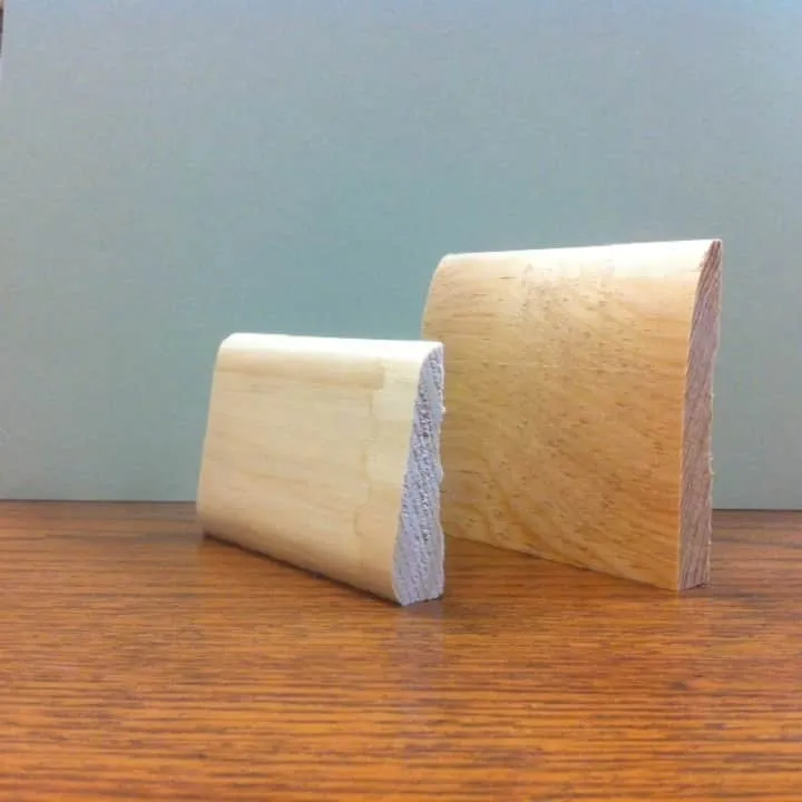 Two wooden baseboard samples on a wood surface, against a light green wall.