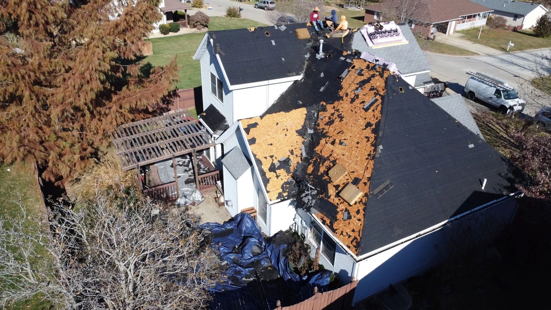 House roof being repaired; workers removing old shingles. Partial roofing replacement in progress.