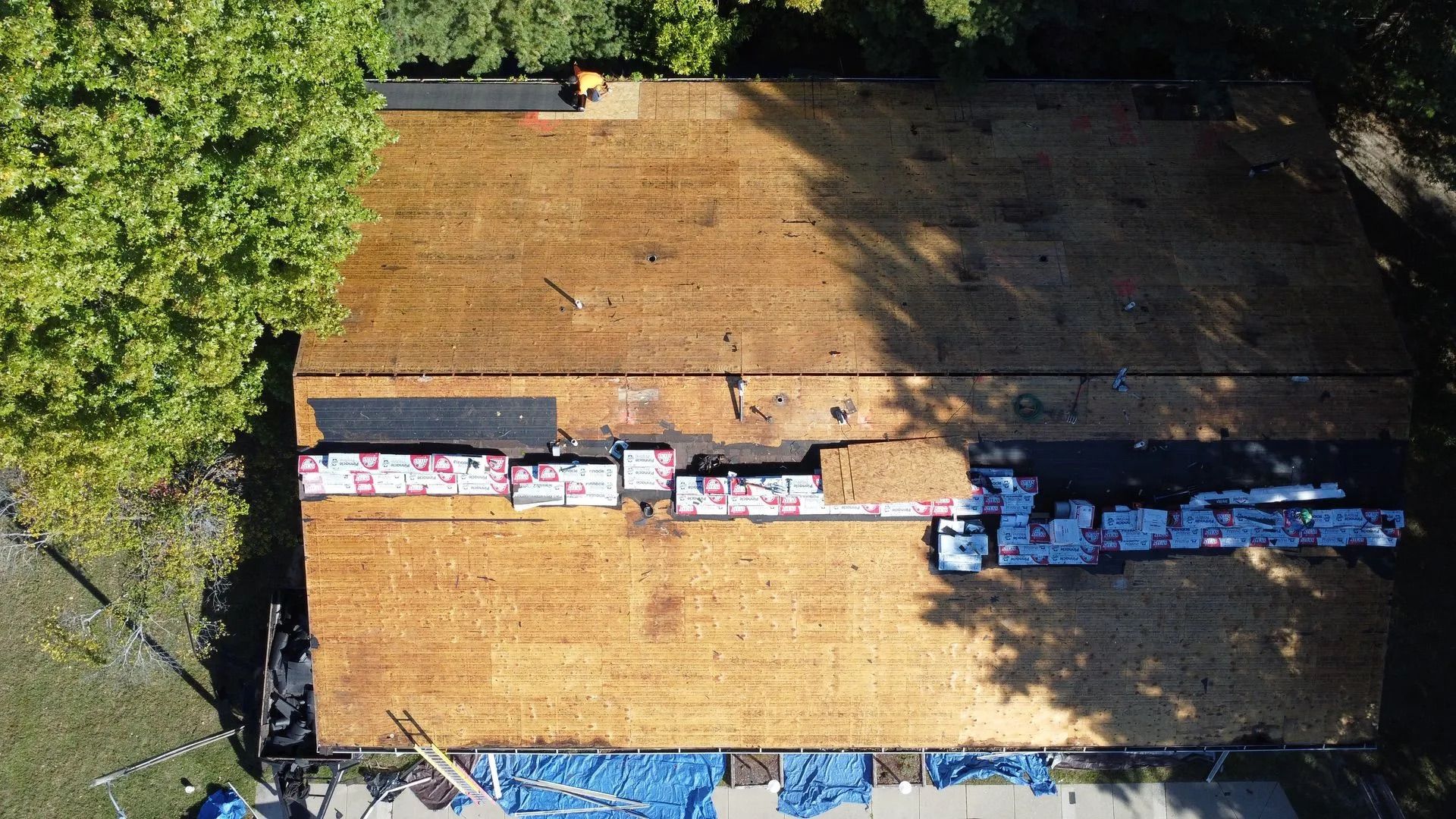 Roofing project: roof partially stripped, bundles of shingles staged, aerial view.