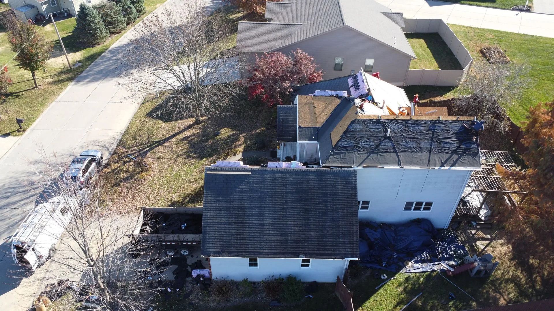 Aerial view of a house with damaged roof and construction materials, possibly a re-roofing project.
