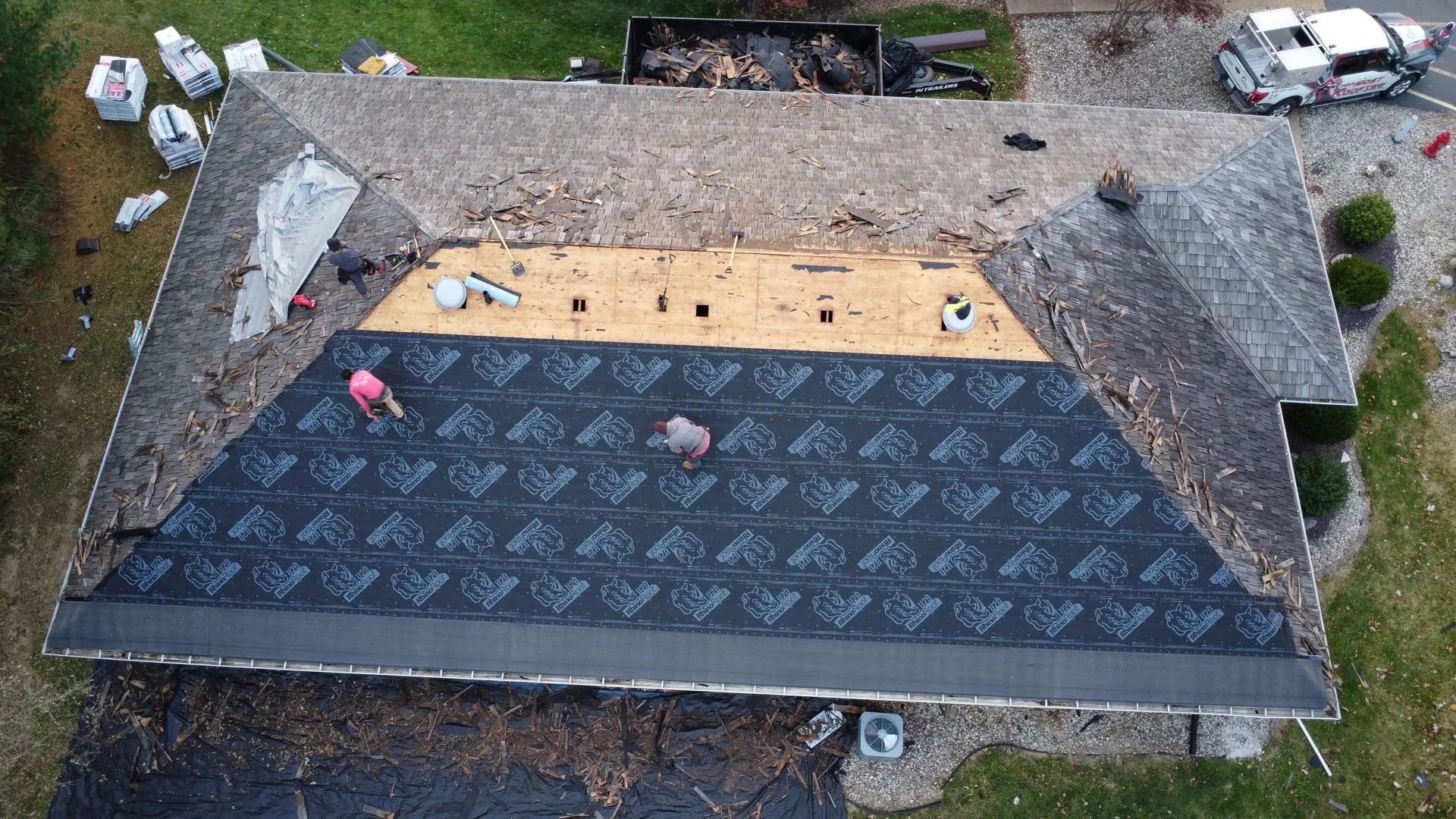 Overhead view of a house roof partially covered with black shingles, workers installing.