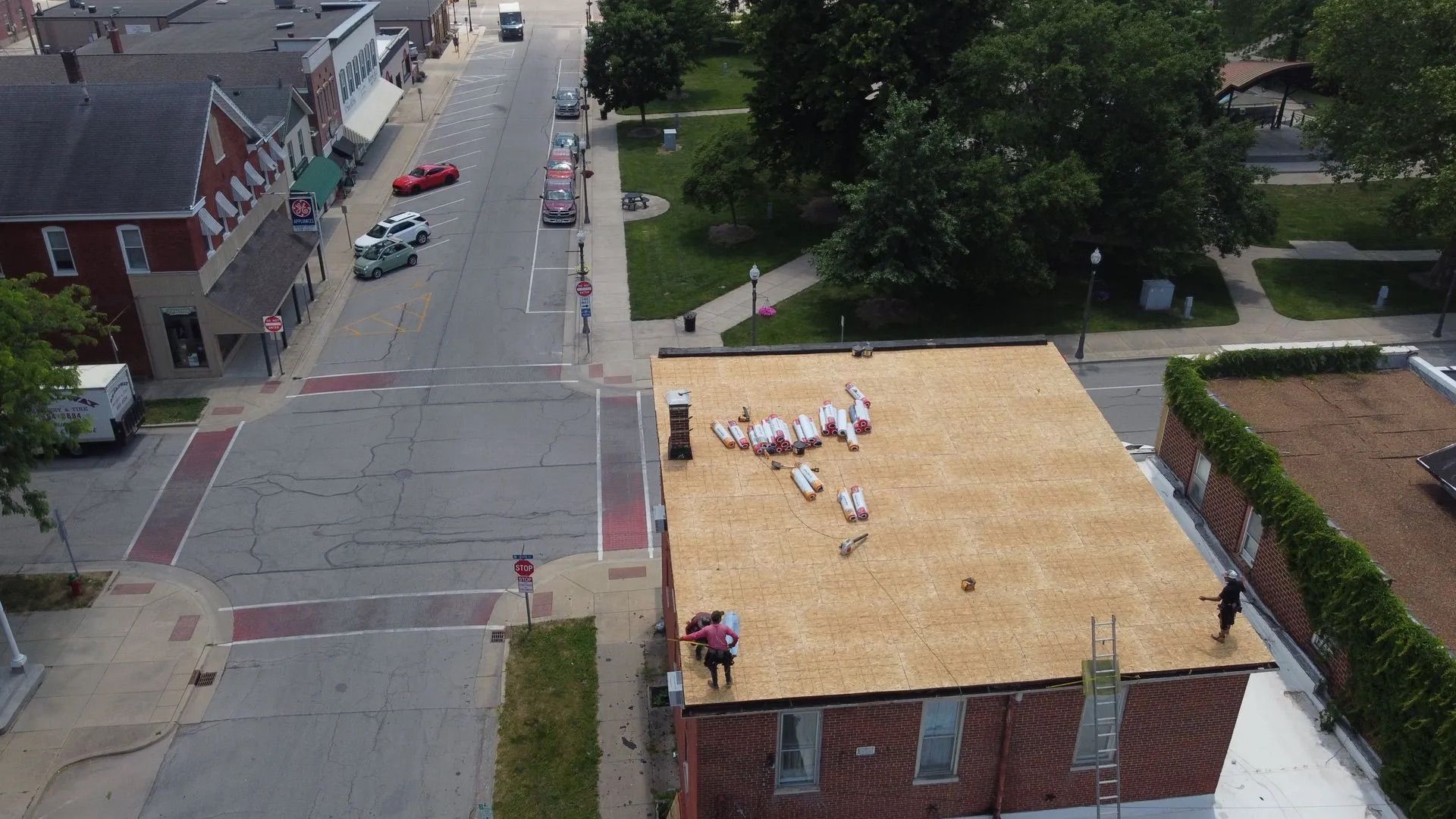 People working on a brown rooftop overlooking a street and buildings in a town.