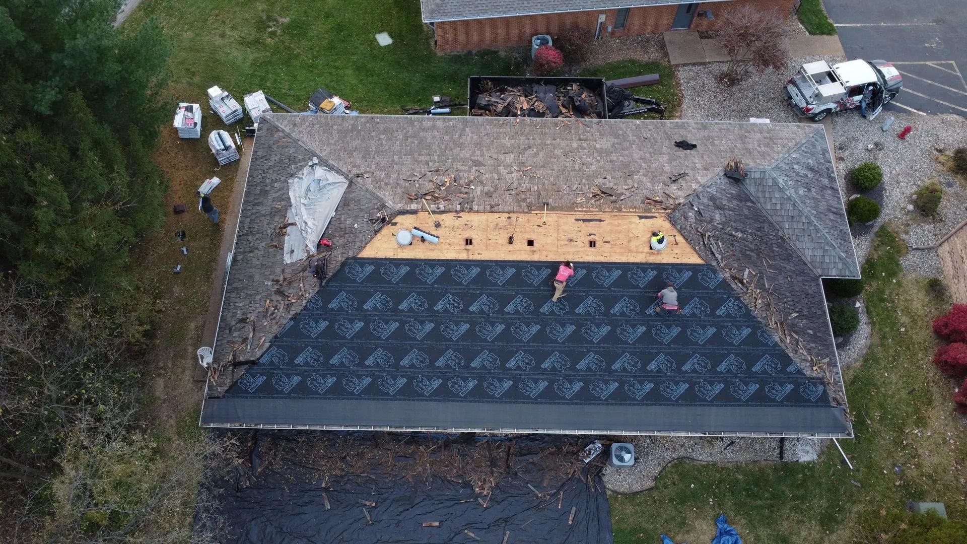 Aerial view of a house roof partially covered with new shingles. Two workers are on the roof.