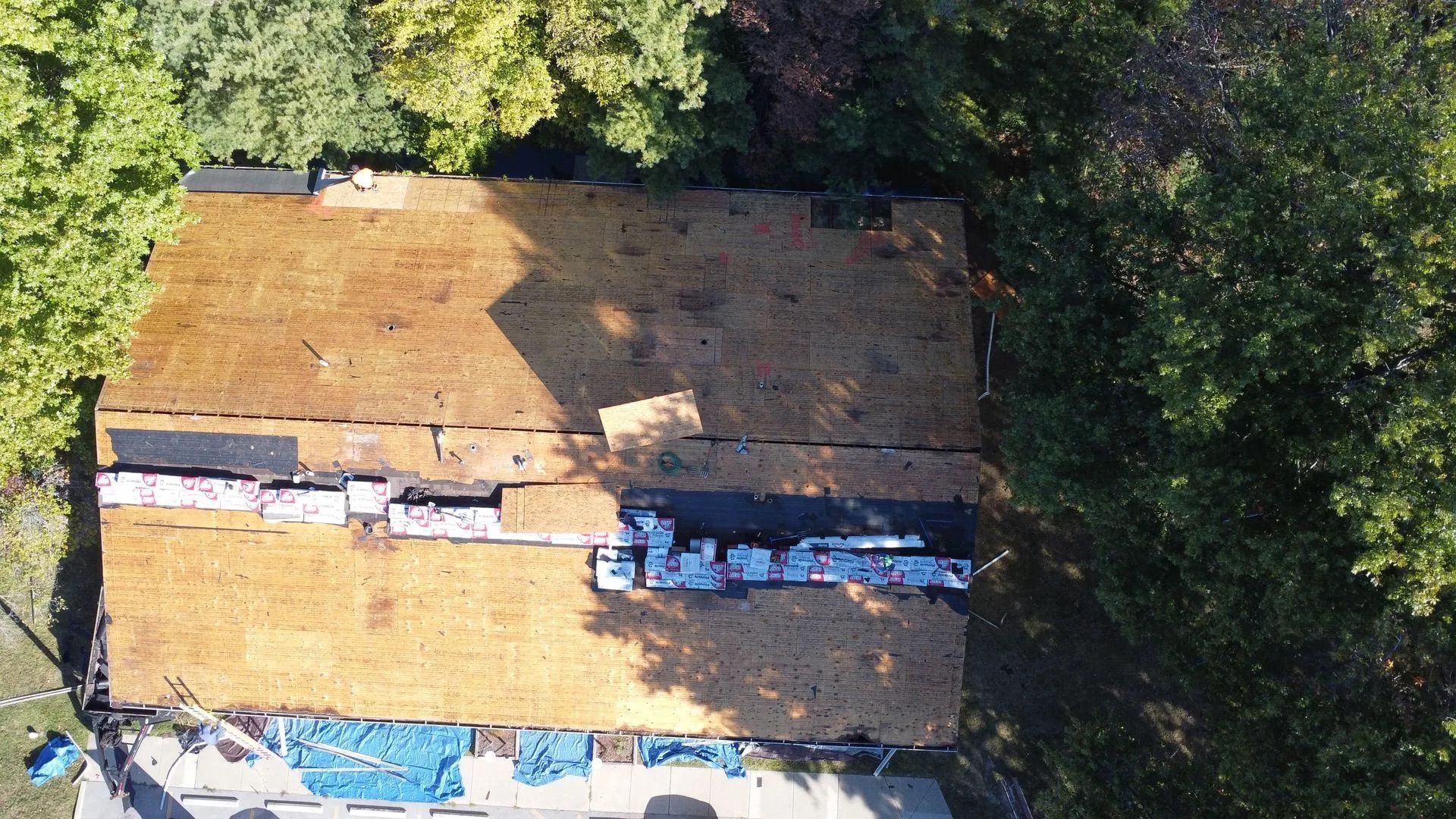 Aerial view of a roof being repaired, with exposed underlayment and shingles. Surrounded by green trees.