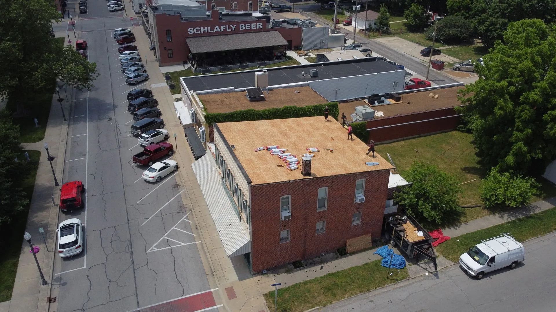 Aerial view of a city street with a red brick building under roof repair; cars parked on the street.
