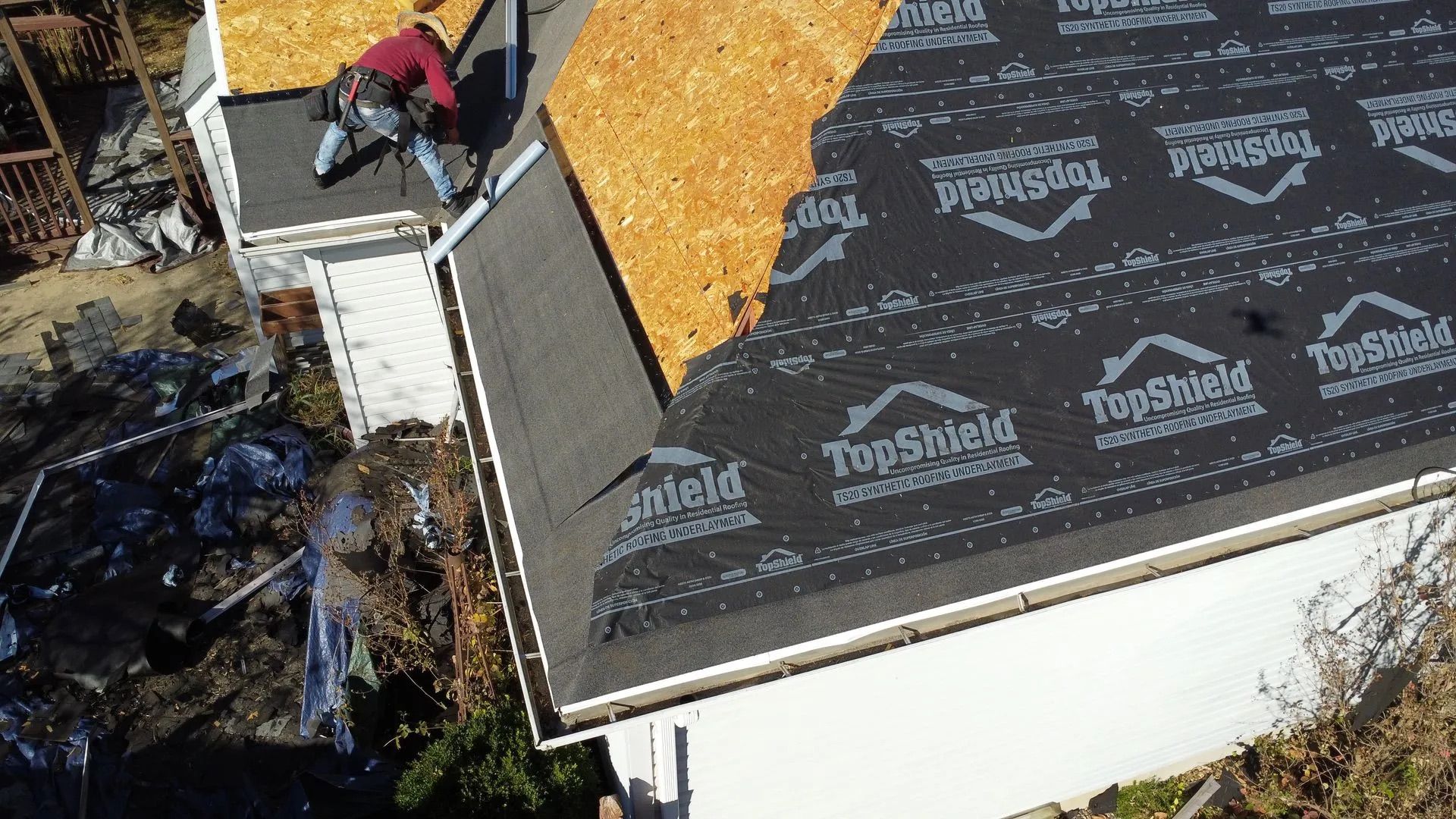 Roofer on a house roof partially covered in new shingles and black underlayment; construction site.
