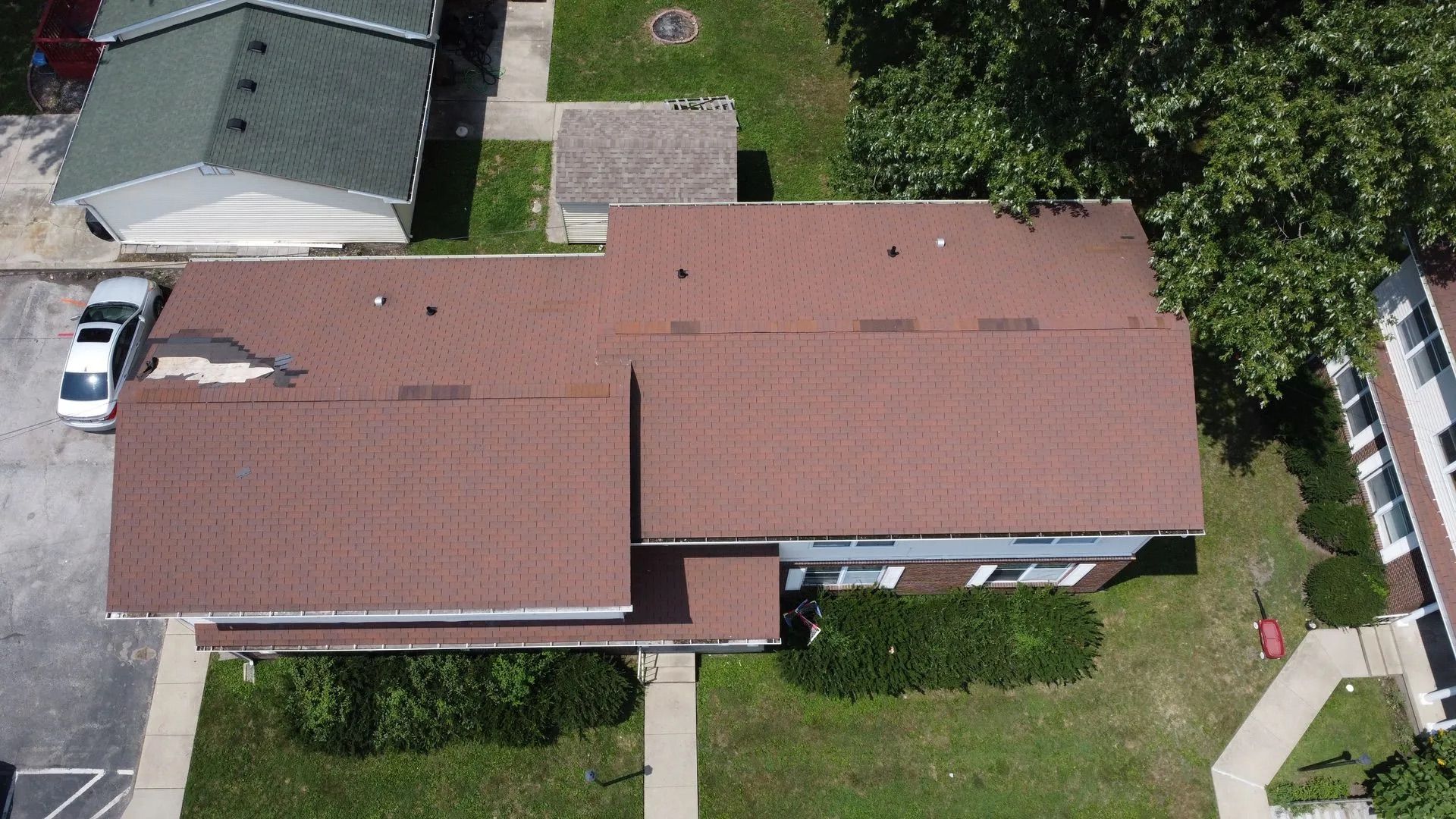 Aerial view of a brown-roofed building and surrounding yard with a car parked next to it.