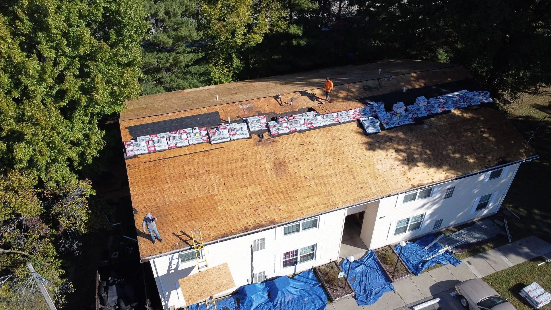Workers replacing a roof on a two-story building; materials and tarps are visible.