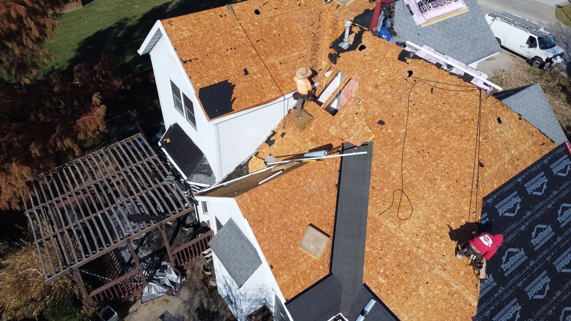 Workers replacing a roof on a white house, seen from above.