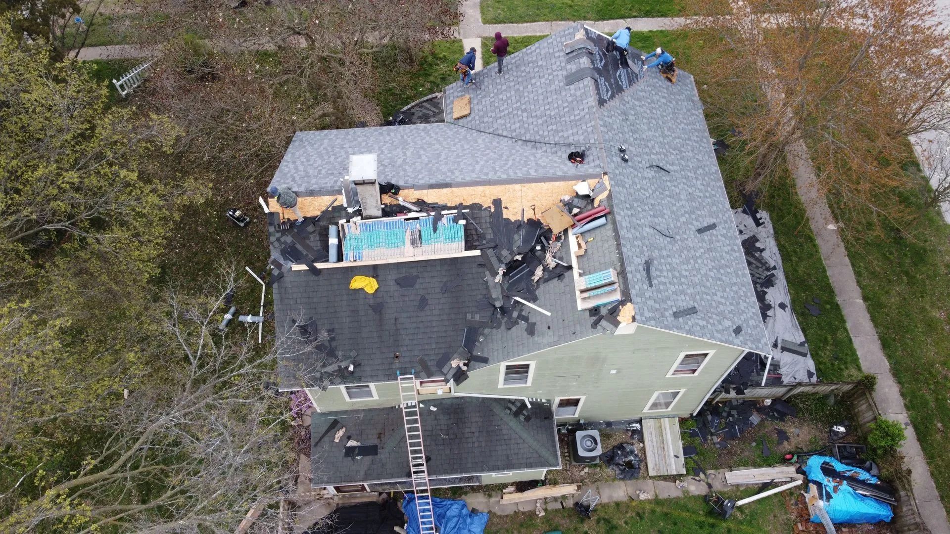 Overhead view of house roof under repair, with workers present and materials visible.