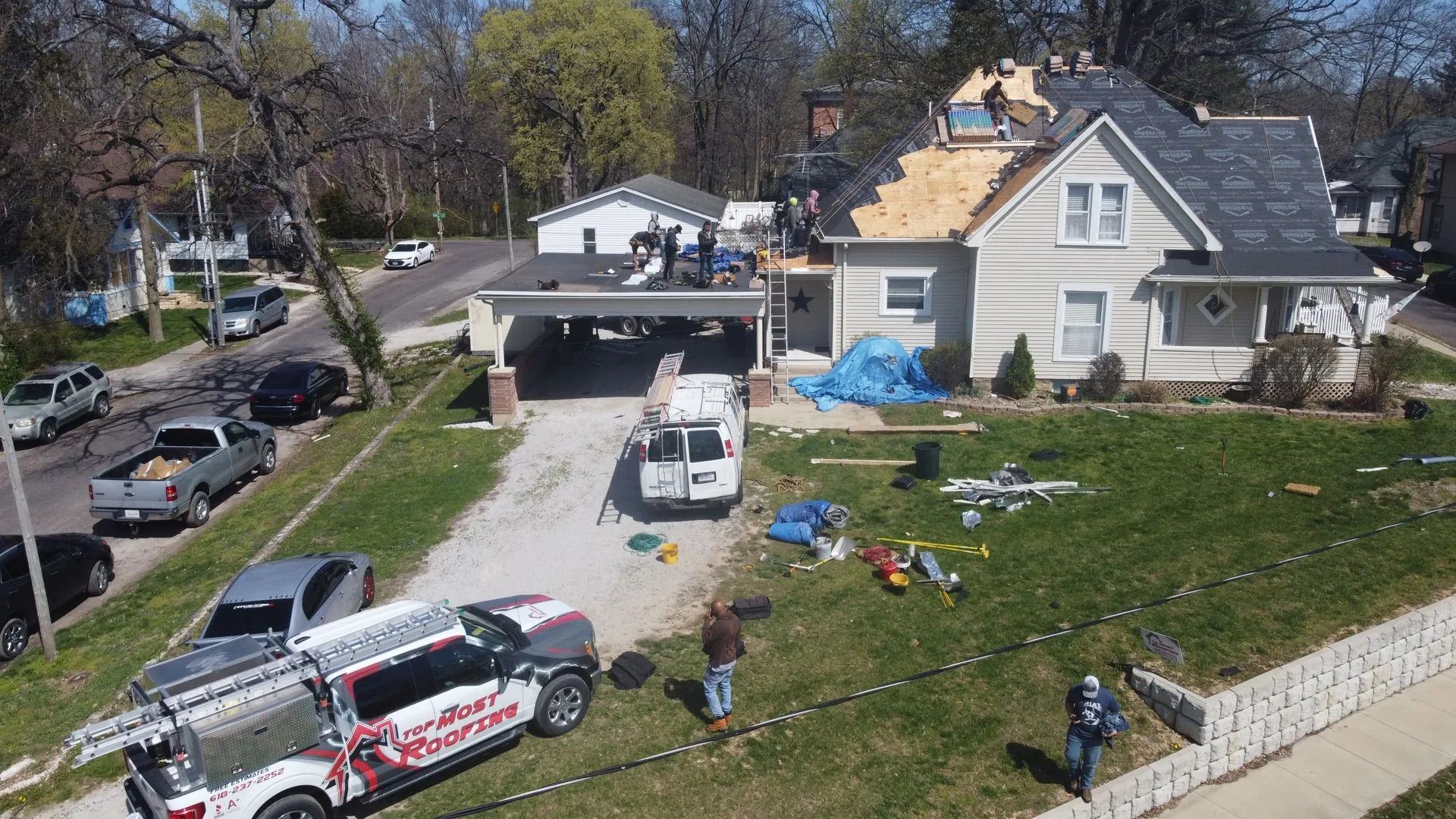 House with roof partially removed during renovation, workers and vehicles present.