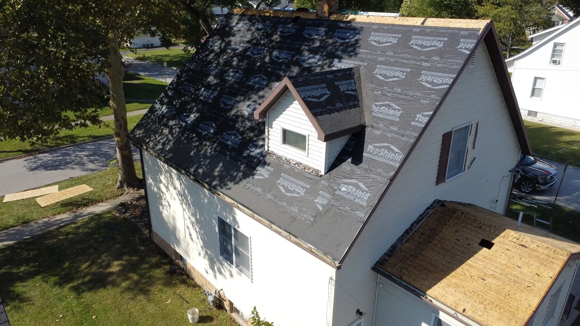 A house with a roof under construction. Gray roofing material and a dormer are visible.