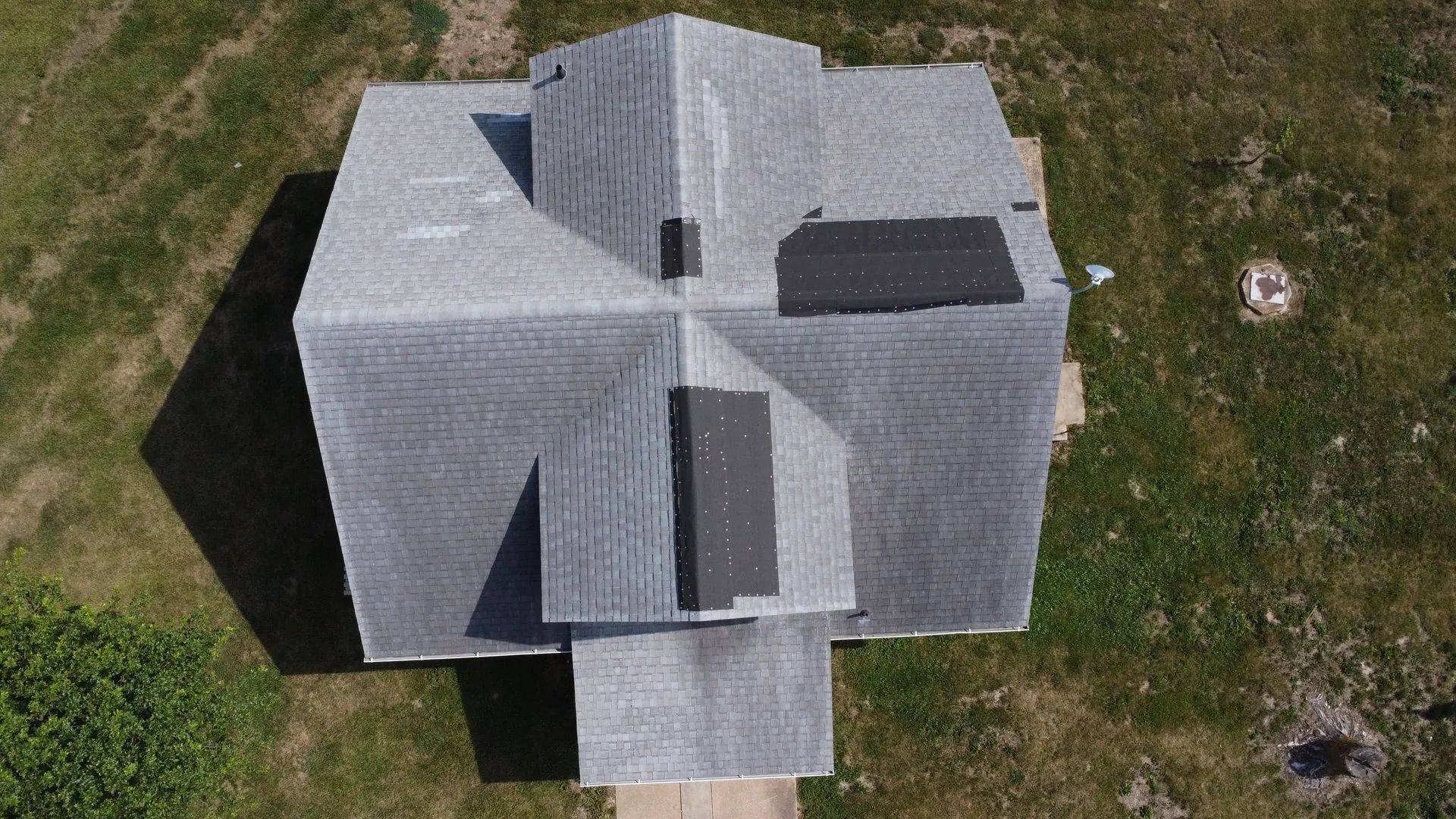 Overhead view of a house with a gray shingled roof, some areas of repair, and a grassy surrounding.