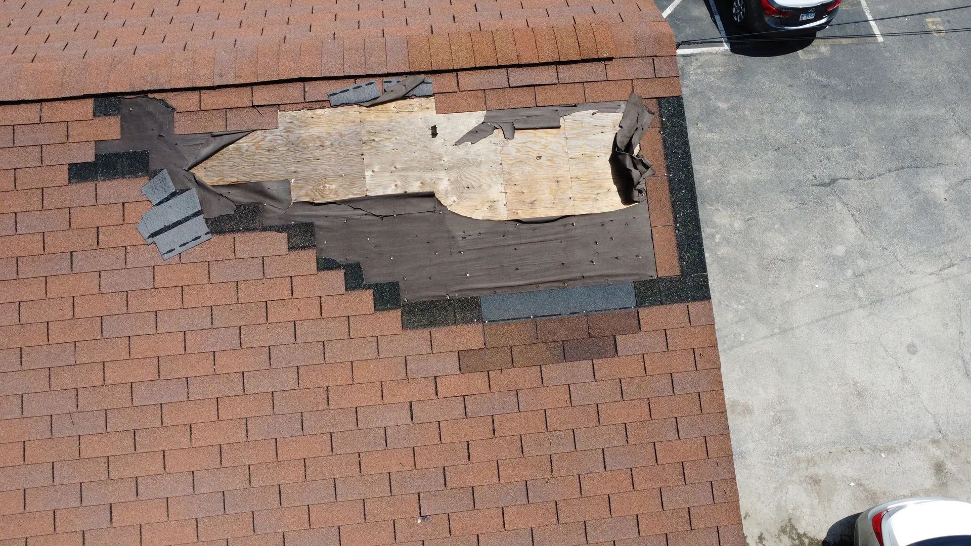 Damaged asphalt shingle roof, large section missing. Brown and black shingles, light wood exposed.