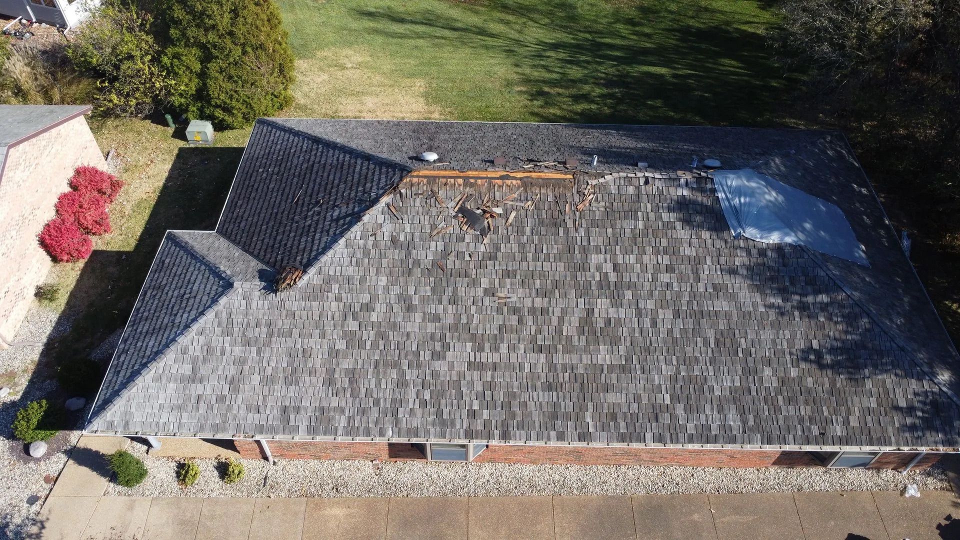 Aerial view of a gray shingle roof with visible damage and a small brick building below.