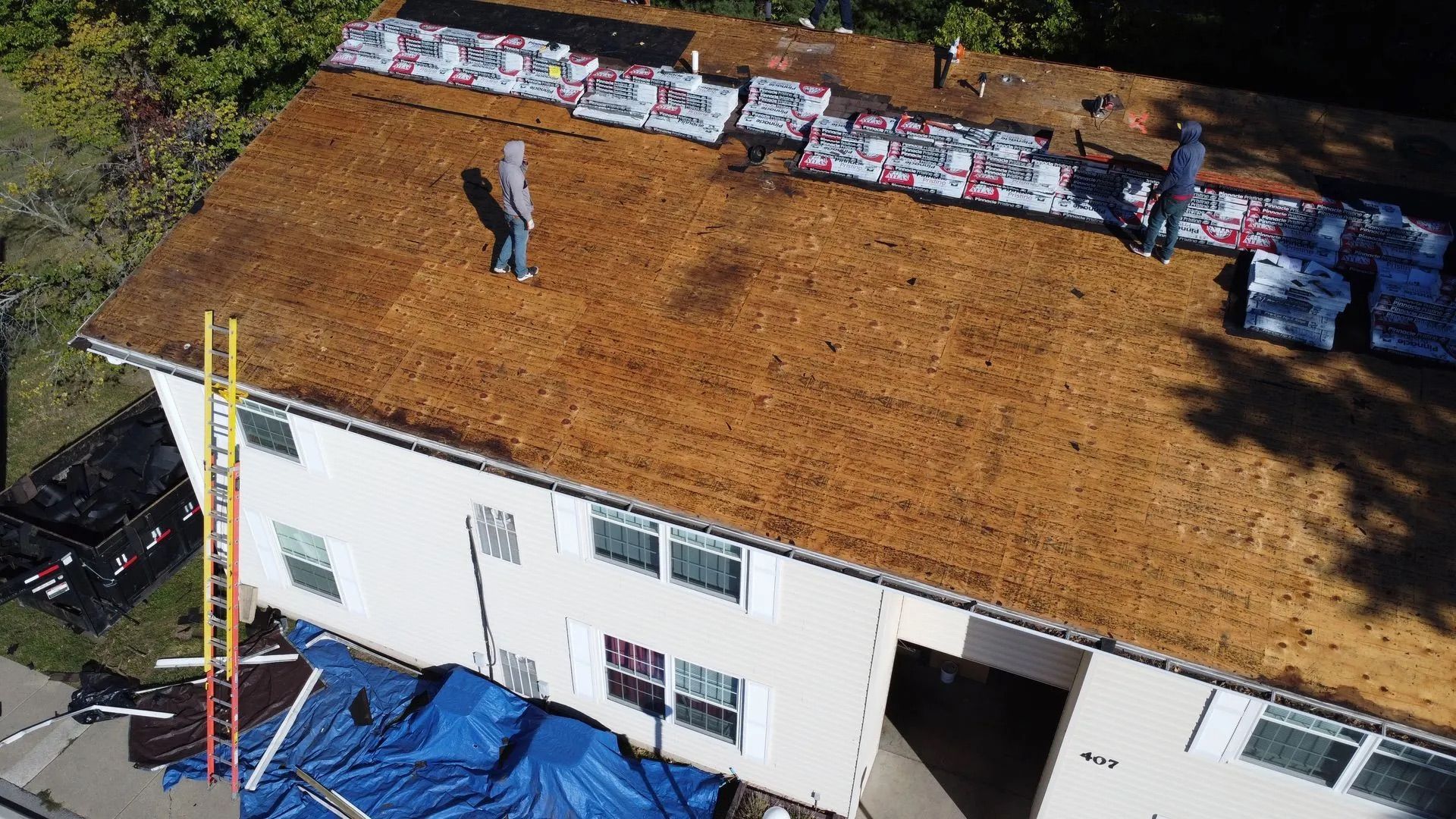 Workers on a rooftop, preparing to install new shingles. Bags of shingles are laid out.